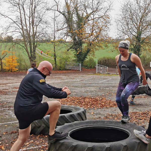 An outdoor bootcamp where members are stepping on a large tractor tyre