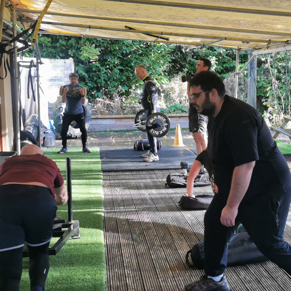 A group of customers exercising on the gym decking, lifting weights, pushing a sledge and doing lunges.