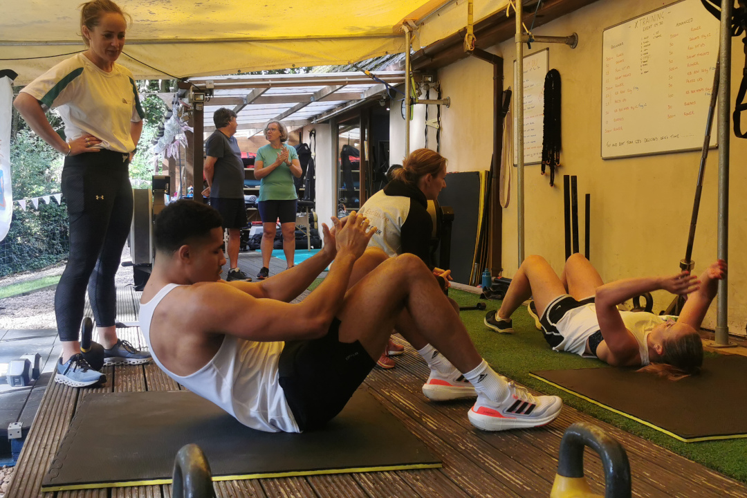 Two people doing abdominal exercises whilst being instructed by personal trainers