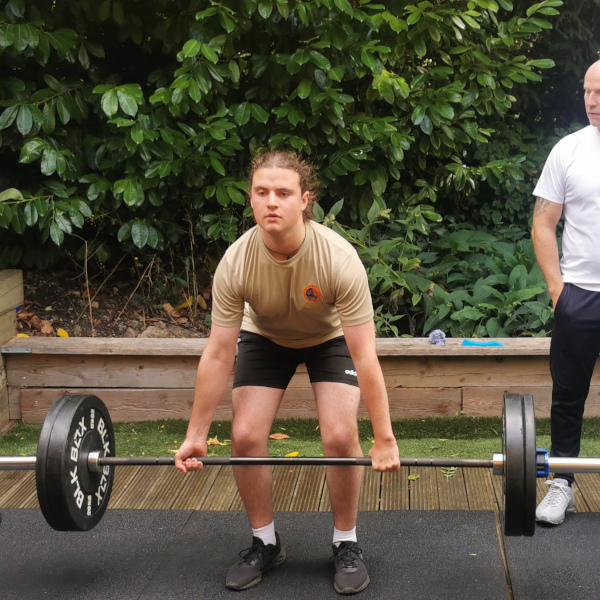 A gym member lifting a barbell under instruction from a personal trainer